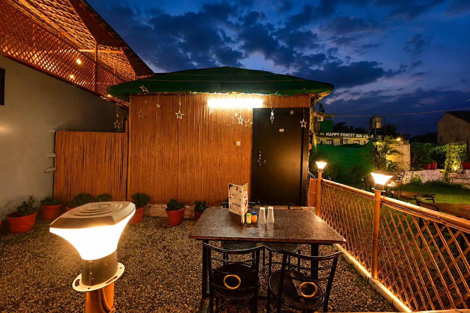 An outdoor patio with a table and chairs, a wooden fence, and a sign for Happy Forest Inn Villa.
