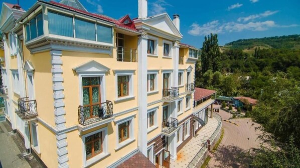 Un edificio de varios pisos con balcones, techo rojo y vista a un paisaje montañoso.