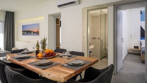 Un comedor moderno con una mesa de madera dispuesta para cuatro personas, rodeada de sillas. Hay un frutero con naranjas y una botella de vino sobre la mesa.