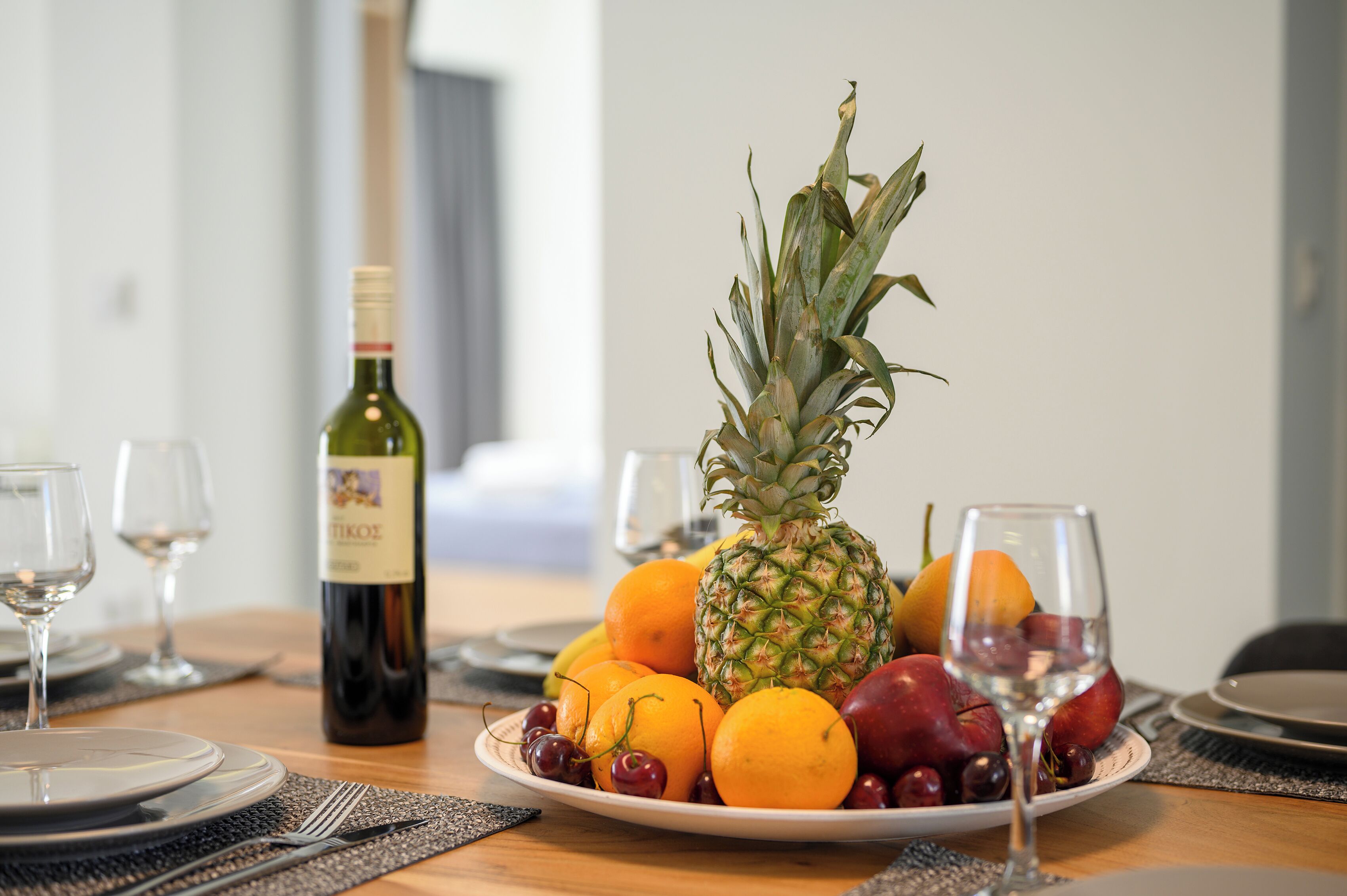 A dining table with a plate of fruit, a bottle of wine, and wine glasses.