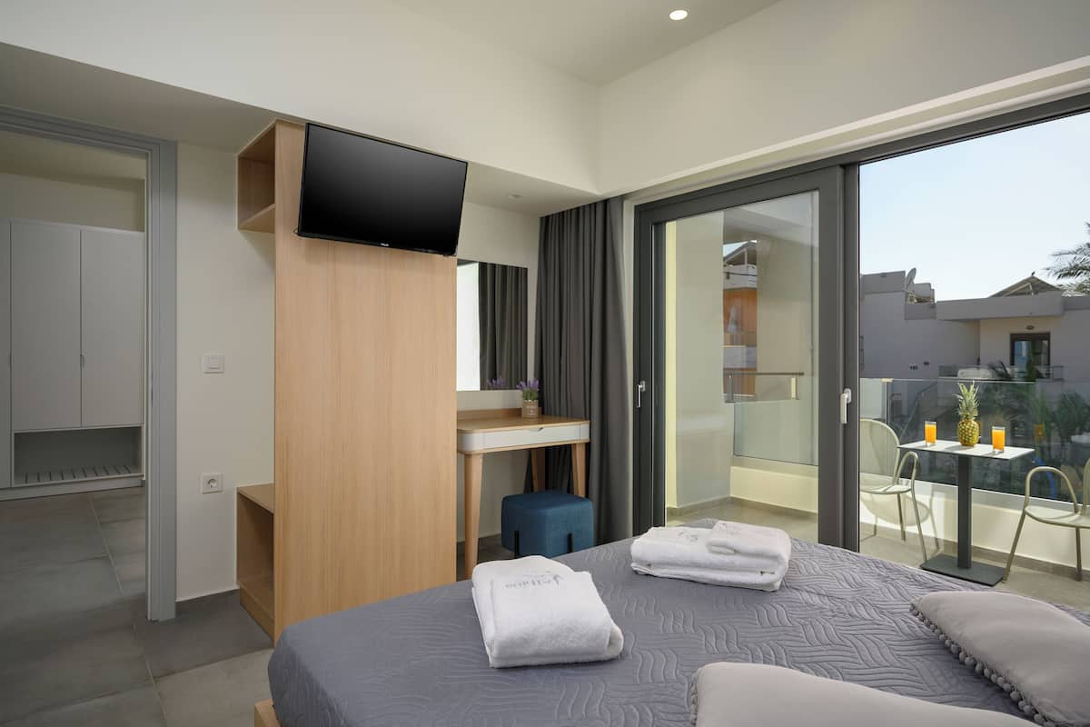 Ett modernt hotellrum med en säng, ett skrivbord, en TV och en balkong med ett bord och stolar.