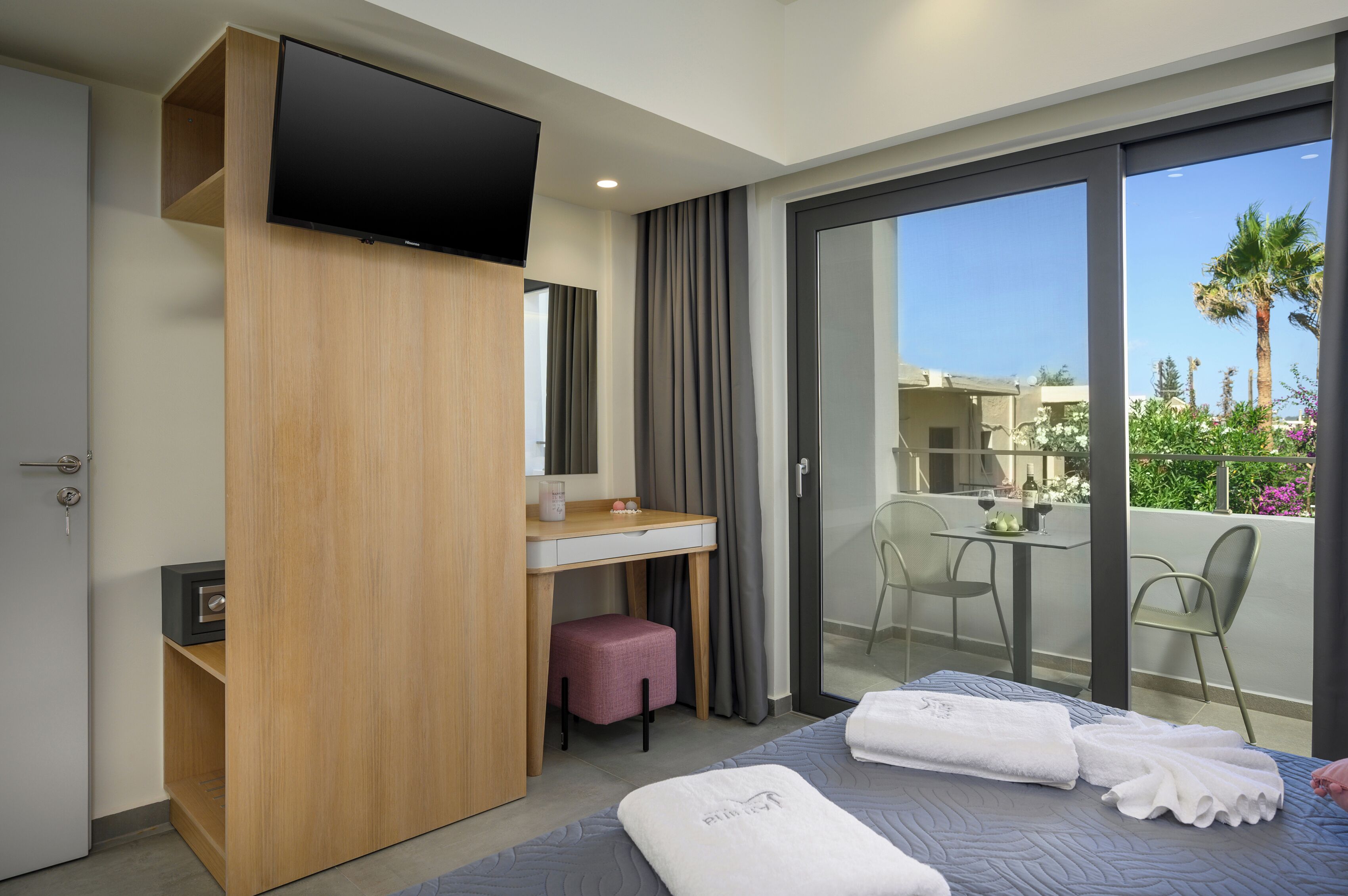 A hotel room with a bed, a desk, a television, and a balcony with chairs and a table.