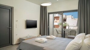 Habitación de hotel moderna con una cama grande, un televisor de pantalla plana en la pared, una mesita auxiliar y un balcón con vistas a la ciudad.