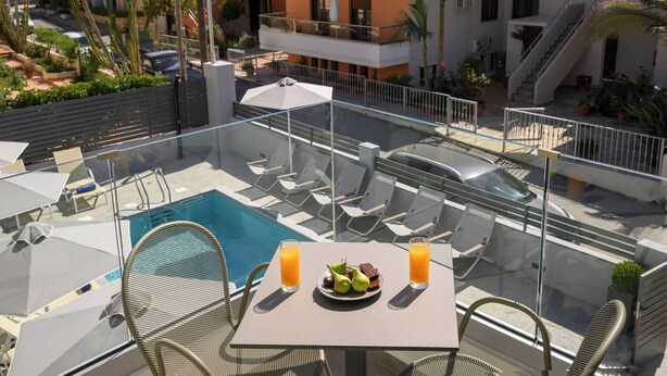 Un área de piscina en la azotea con una mesa para dos, que incluye un plato de fruta y dos vasos de zumo de naranja.