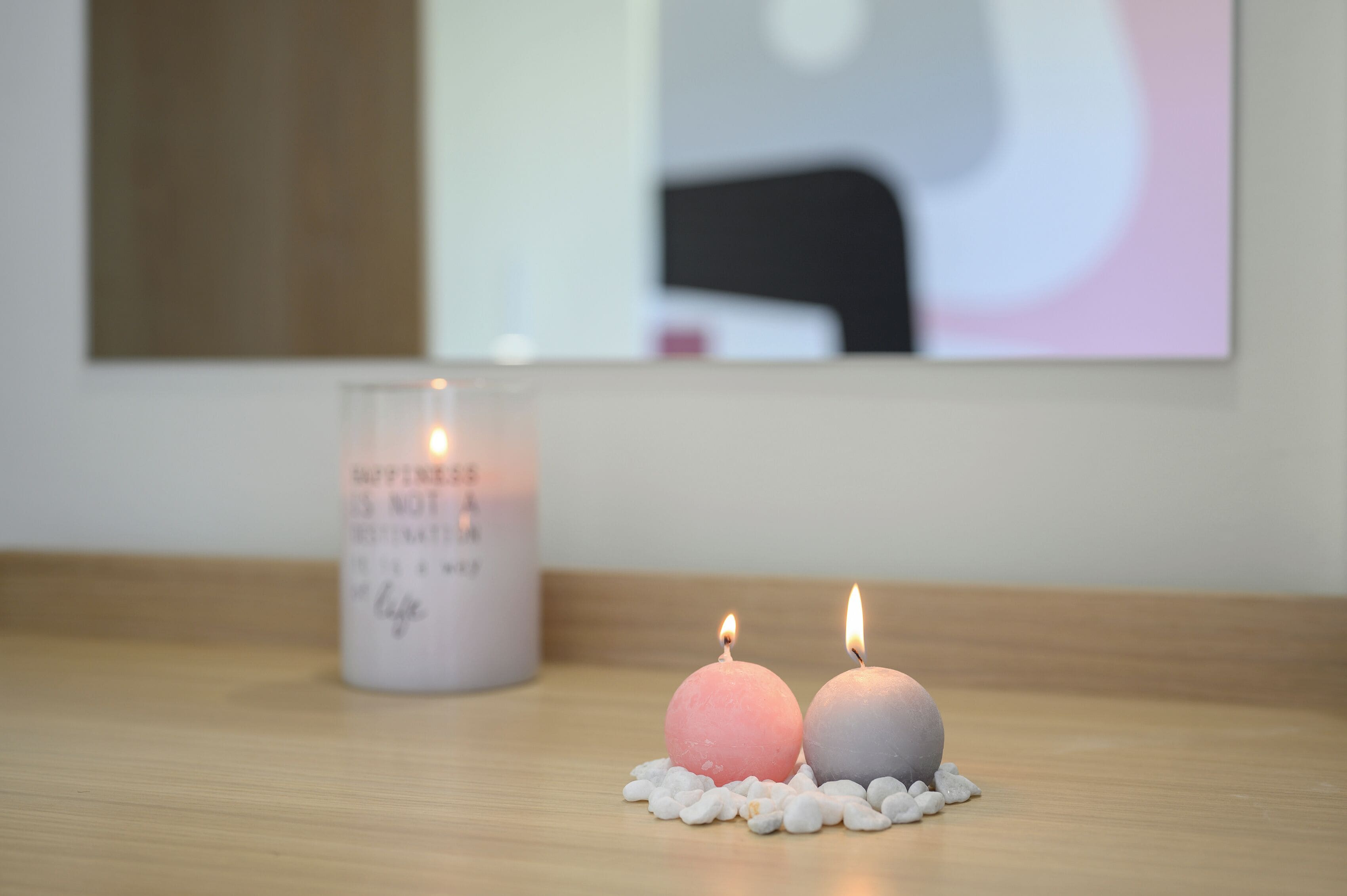 Two lit candles on a wooden surface with a candle holder in the background.