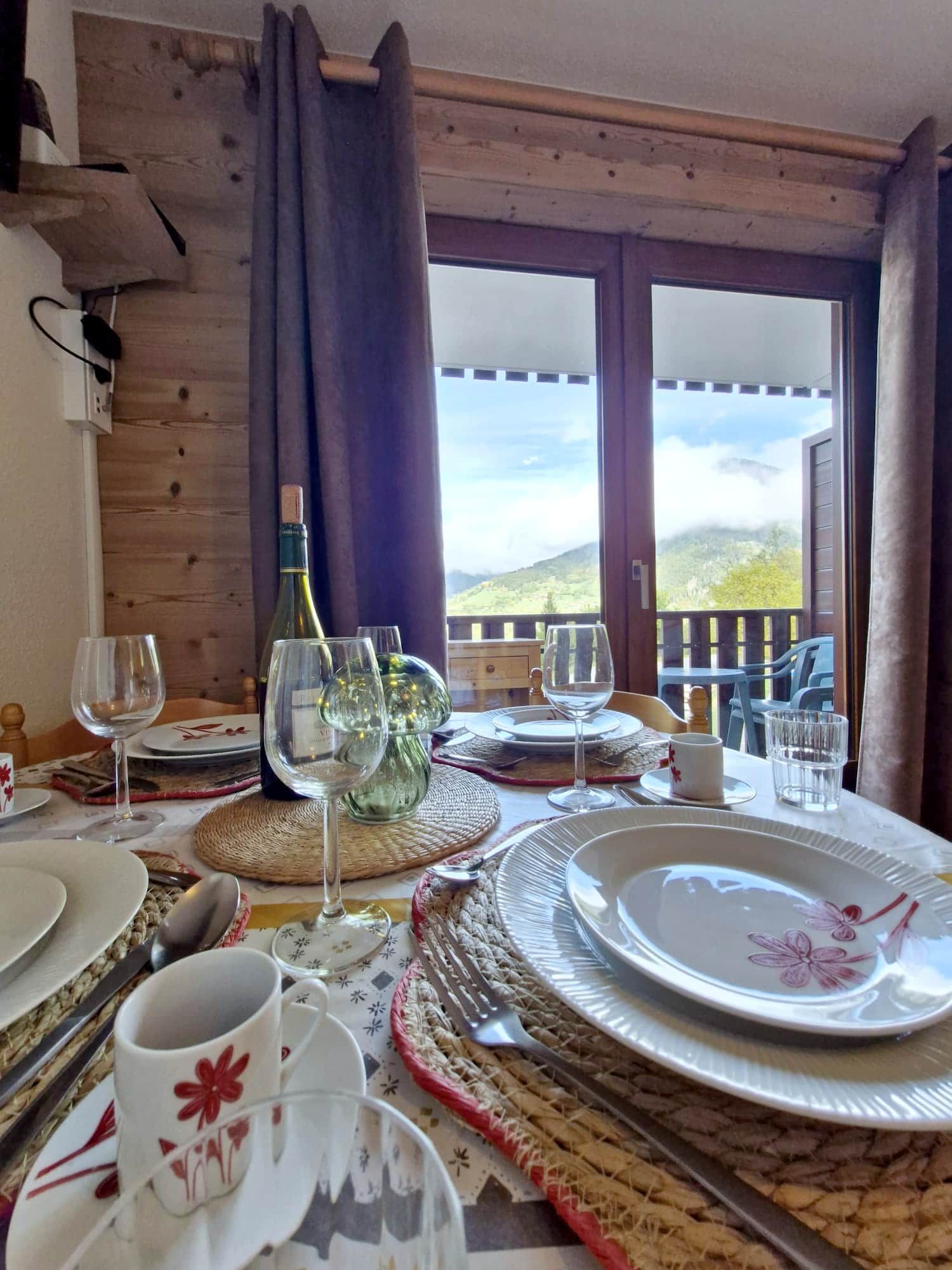 A dining table set with plates, glasses, and a bottle, overlooking a scenic view.