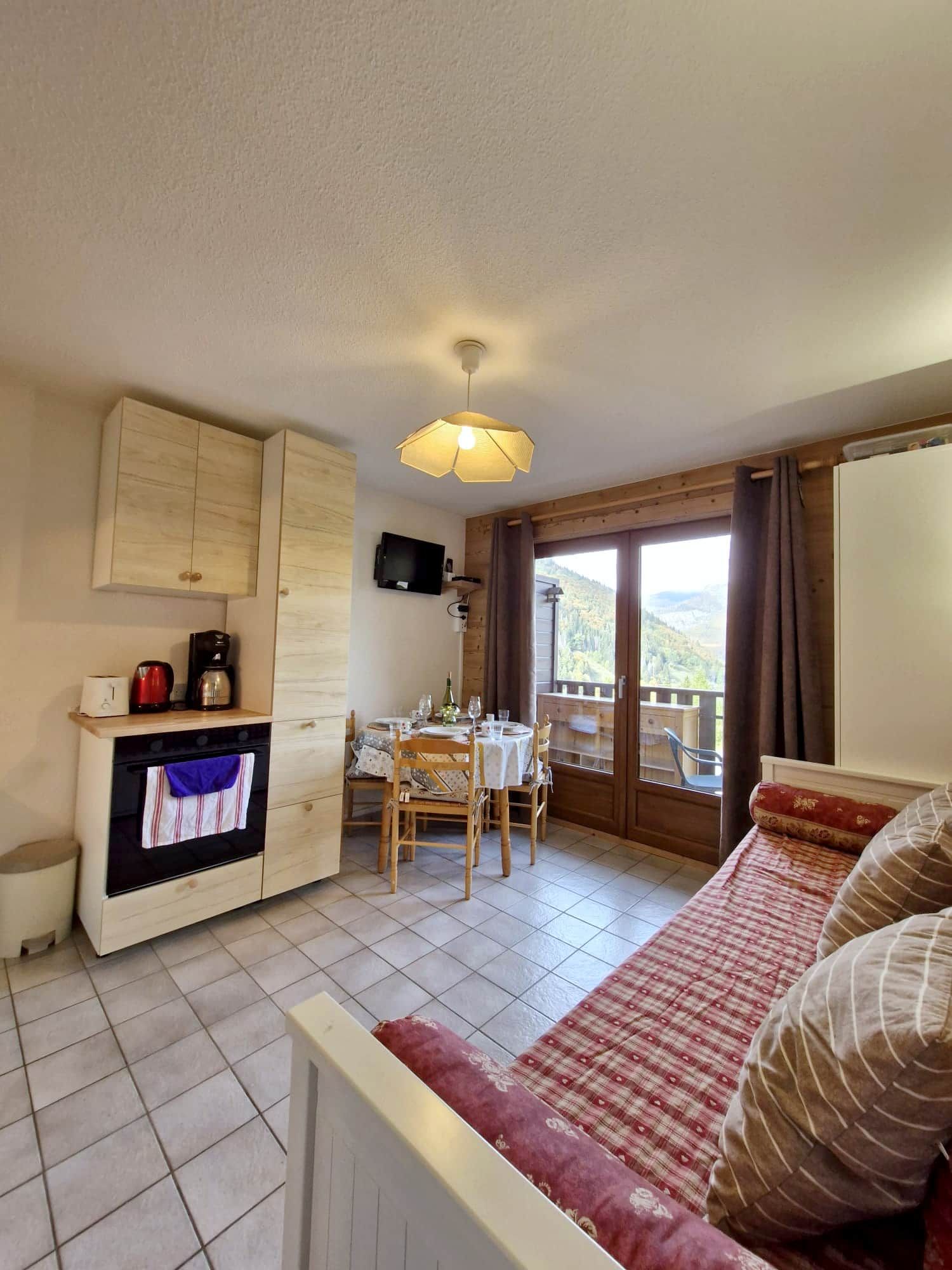 A cozy room with a sofa, a dining table with chairs, a television, and a view of the outdoors.