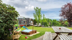 A backyard with a wooden playset, a picnic table, and a view of a house and landscape. - Apartment "Rachel" with Mountain View, Shared Terrace and Wi-Fi (Perlesreut)