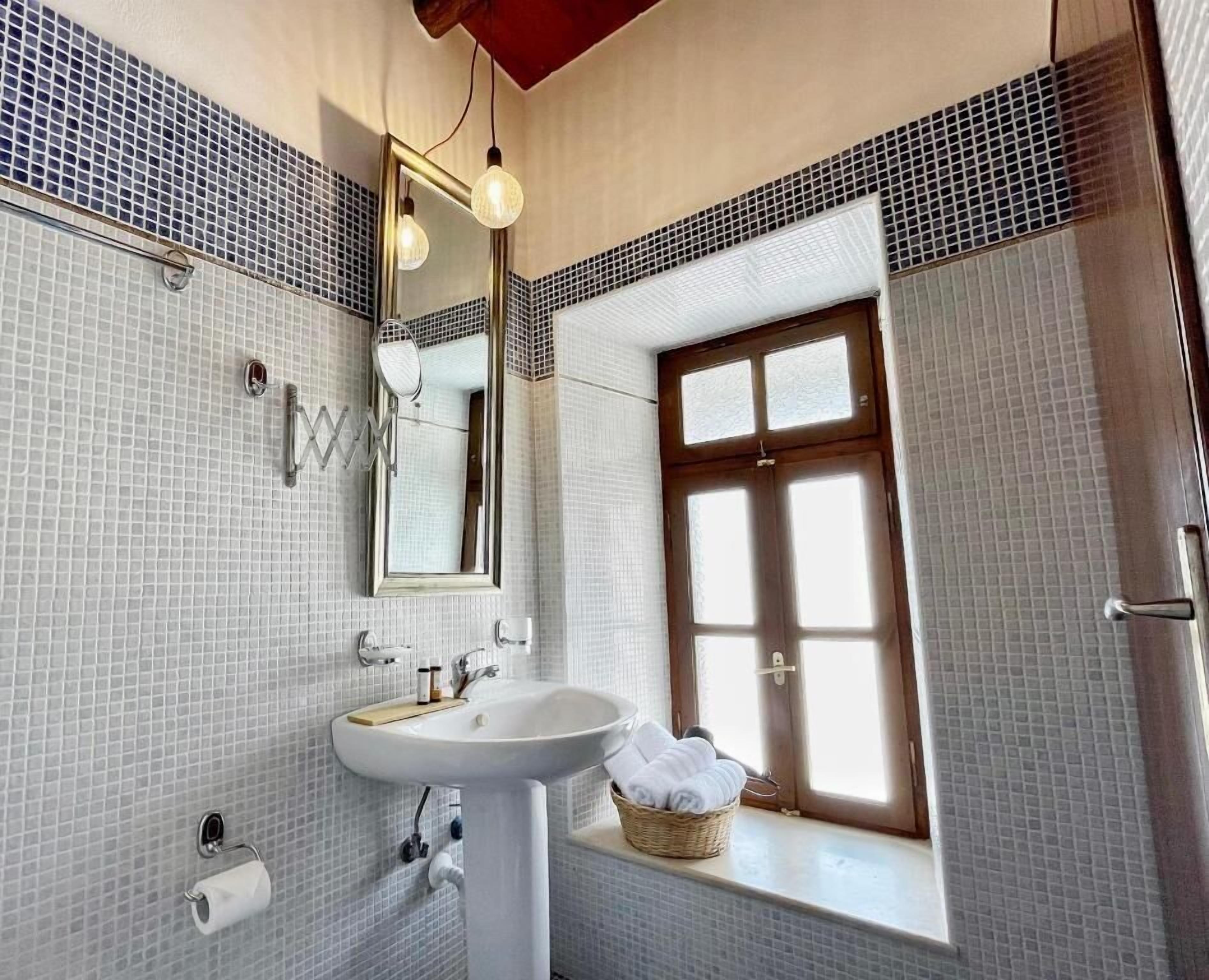 A bathroom with a white sink, a mirror, and a window with a wooden frame.
