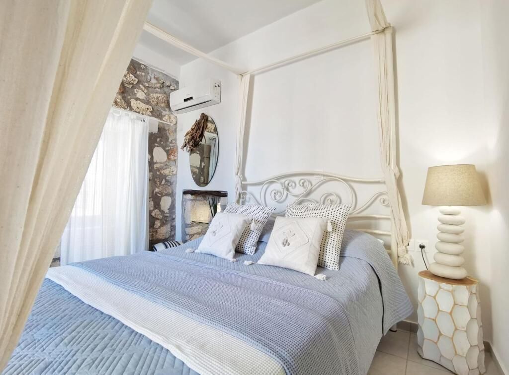 A bedroom with a bed, a nightstand, a lamp, a mirror, and a stone wall.