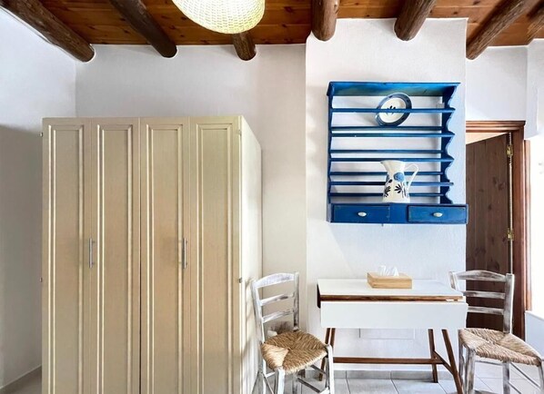 A room with a white wardrobe, a blue shelf unit with decorative items, a white table, and two chairs. - Four Seasons Of Bliss at Sohora Hotel (Rethymno)