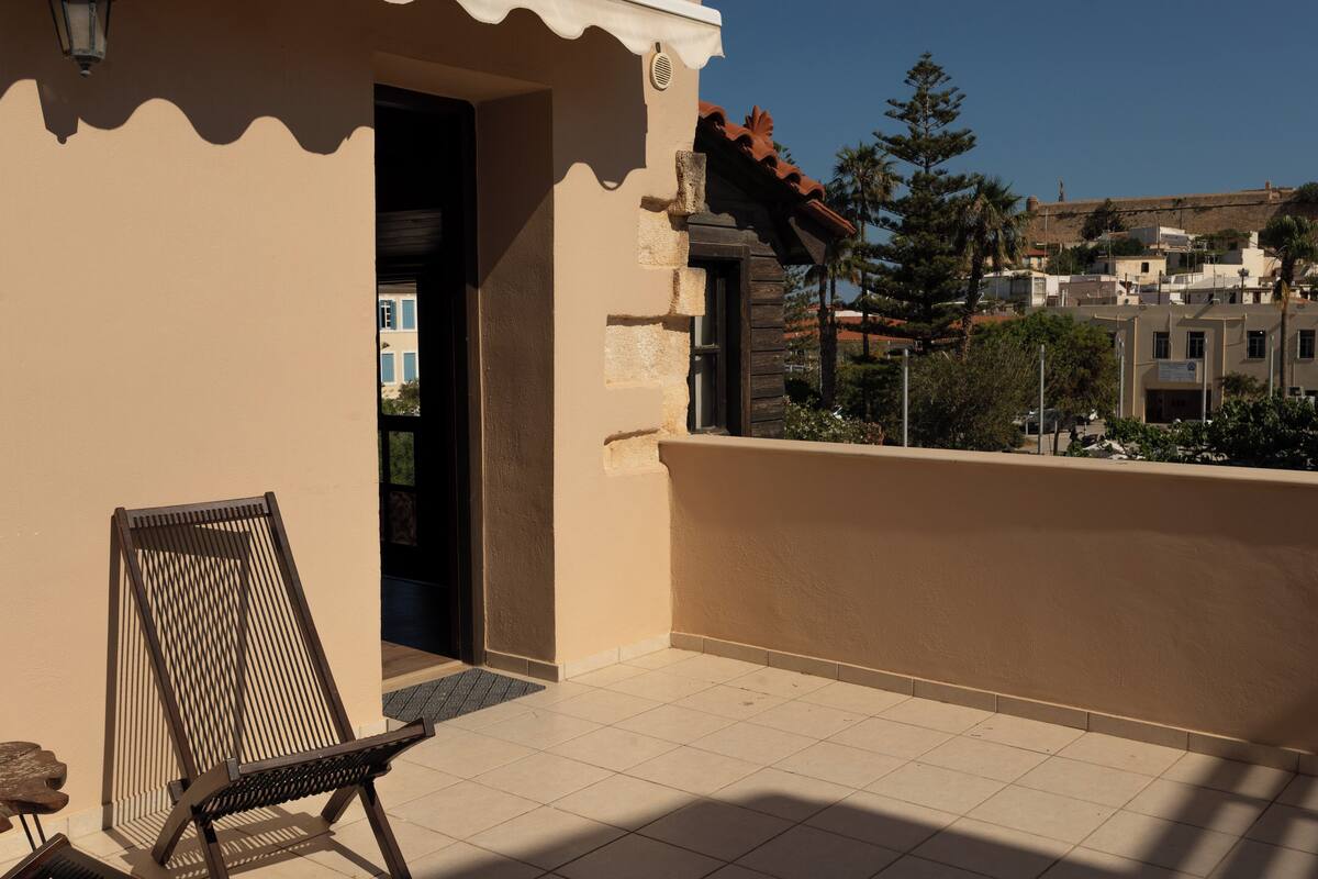Un balcon avec une chaise, une porte et une vue sur des bâtiments au loin.