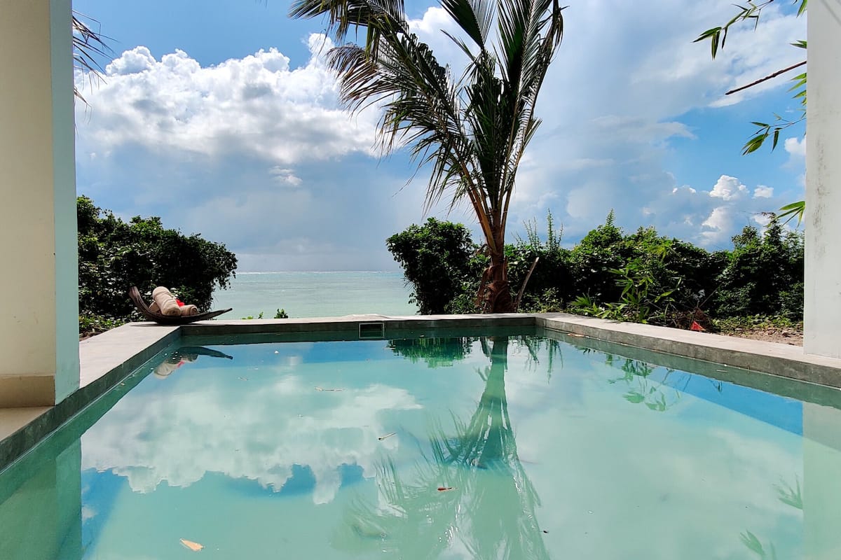 A clear view of a swimming pool with a view of the ocean and palm trees.