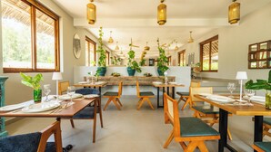 A dining area with wooden tables and chairs, potted plants, and hanging pendant lights. - Legendary Zanzibar Beach Resort (Michamvi)