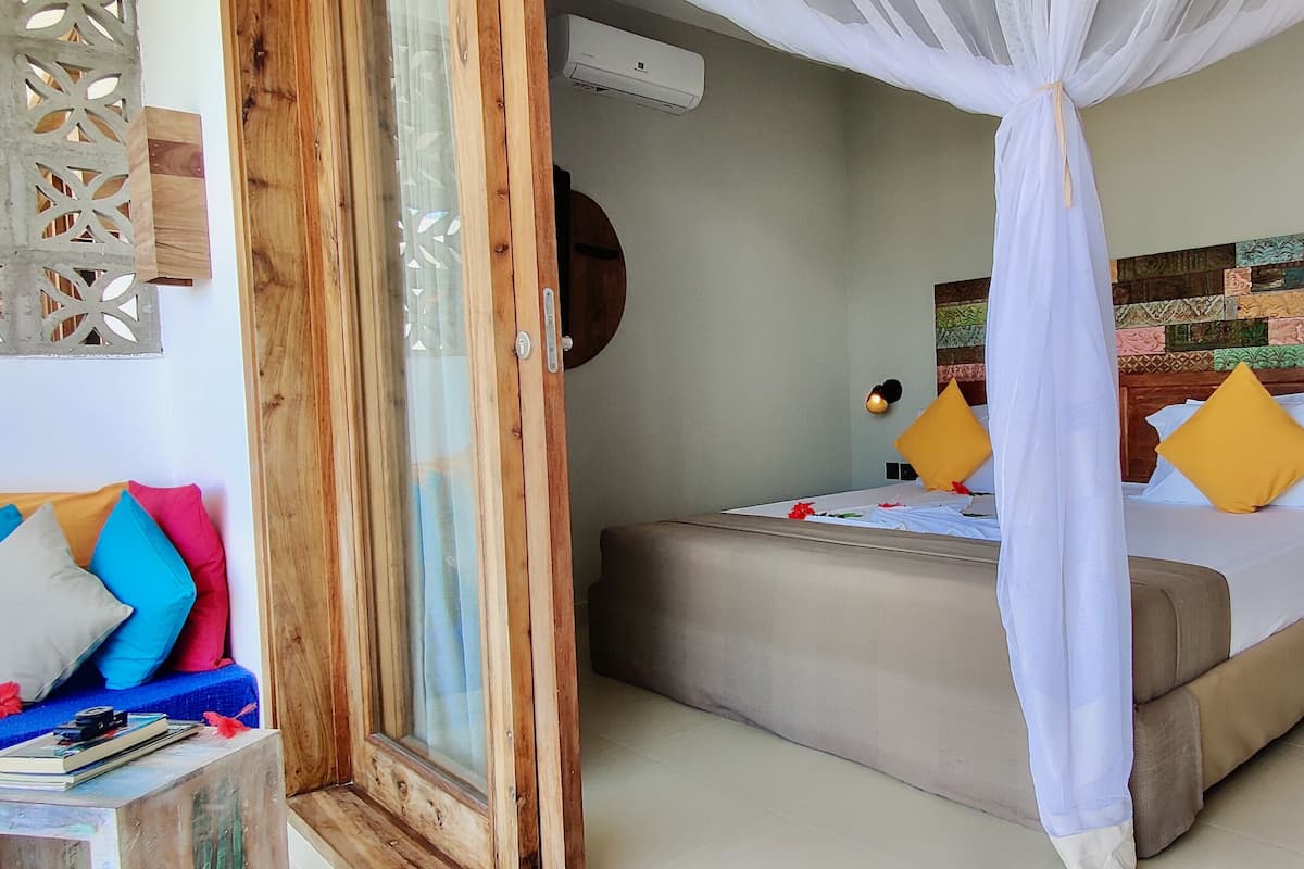 A bedroom with a bed, a bedside table, a nightstand, a wall-mounted air conditioner, and a decorative wall piece.