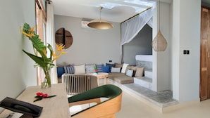 A modern living room with a sofa, a dining table, and a chair. There is a plant on the table and a hanging light fixture. - Legendary Zanzibar Beach Resort (Michamvi)