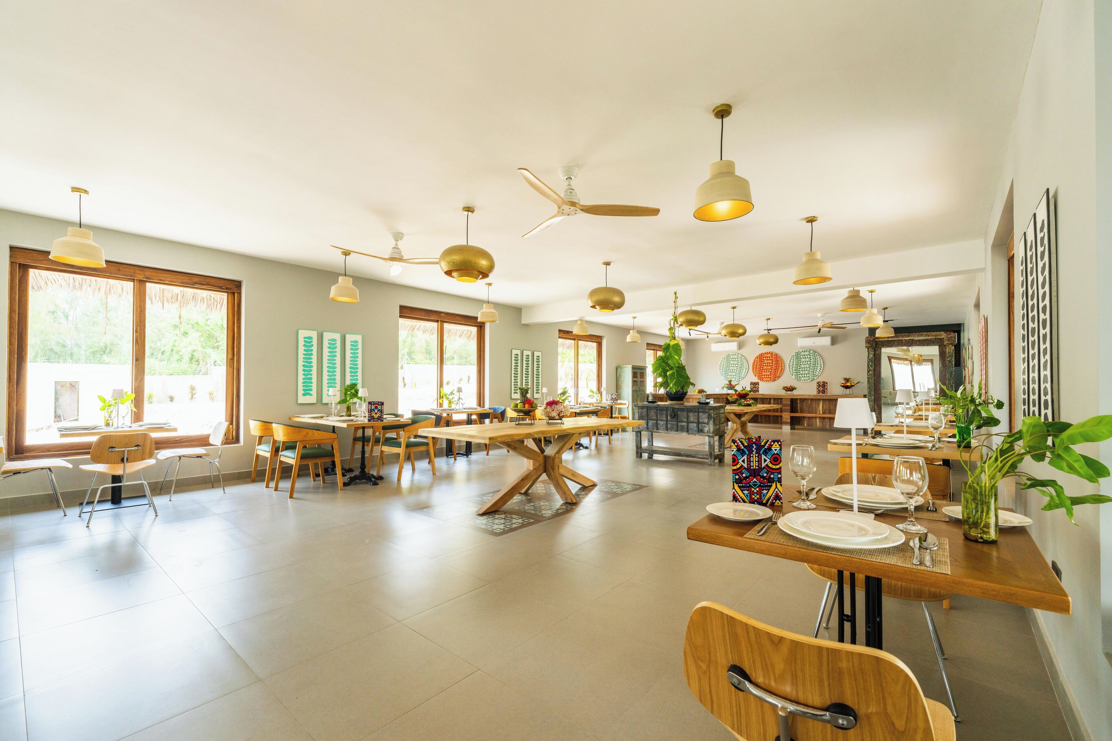 A spacious dining area with multiple tables and chairs, ceiling fans, and large windows allowing natural light.