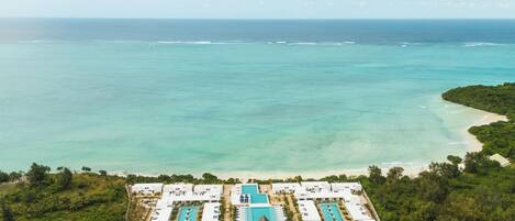 Vista aérea de un complejo turístico con varias piscinas, acceso a la playa y abundante vegetación.