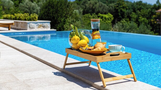 A poolside setting with a tray holding lemons, a glass of water, a croissant, and a cup. - Luxury 4-bedroom Villa with Private Heated Pool & Sea View, near Portonovi. (Đenovići)