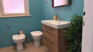 Un baño con inodoro, bidé y lavabo, mueble de madera y un espejo sobre el lavabo.