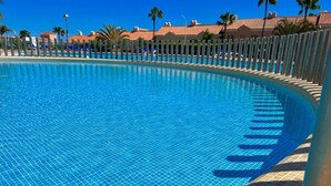 Piscina cristallina blu con bordo piastrellato, circondata da una recinzione e palme.