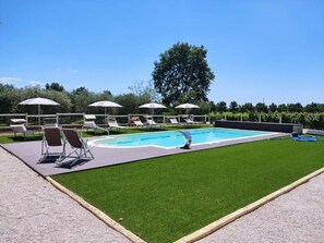 Piscina com espreguiçadeiras e guarda-sóis, rodeada por um relvado bem cuidado e árvores.