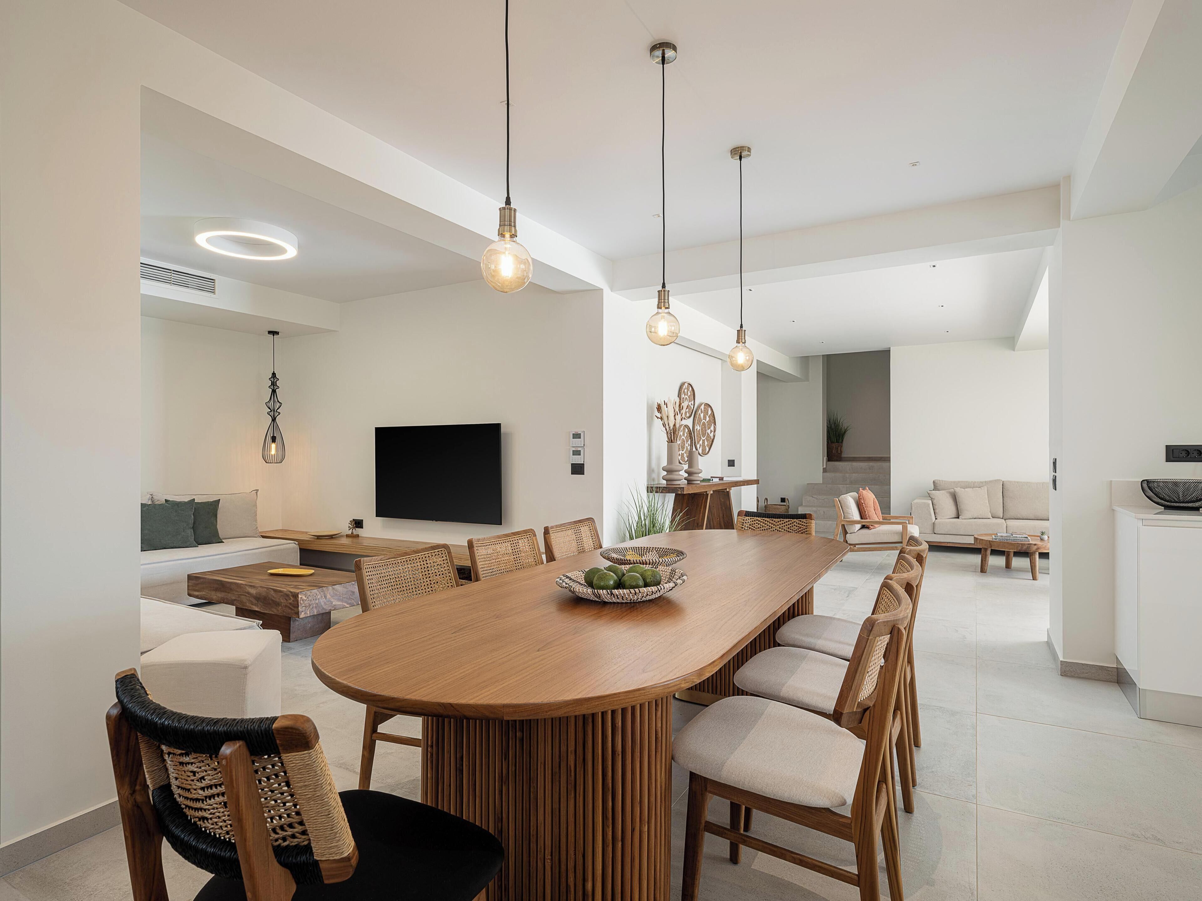 A modern kitchen with a large wooden island, pendant lights, and a flat-screen TV.