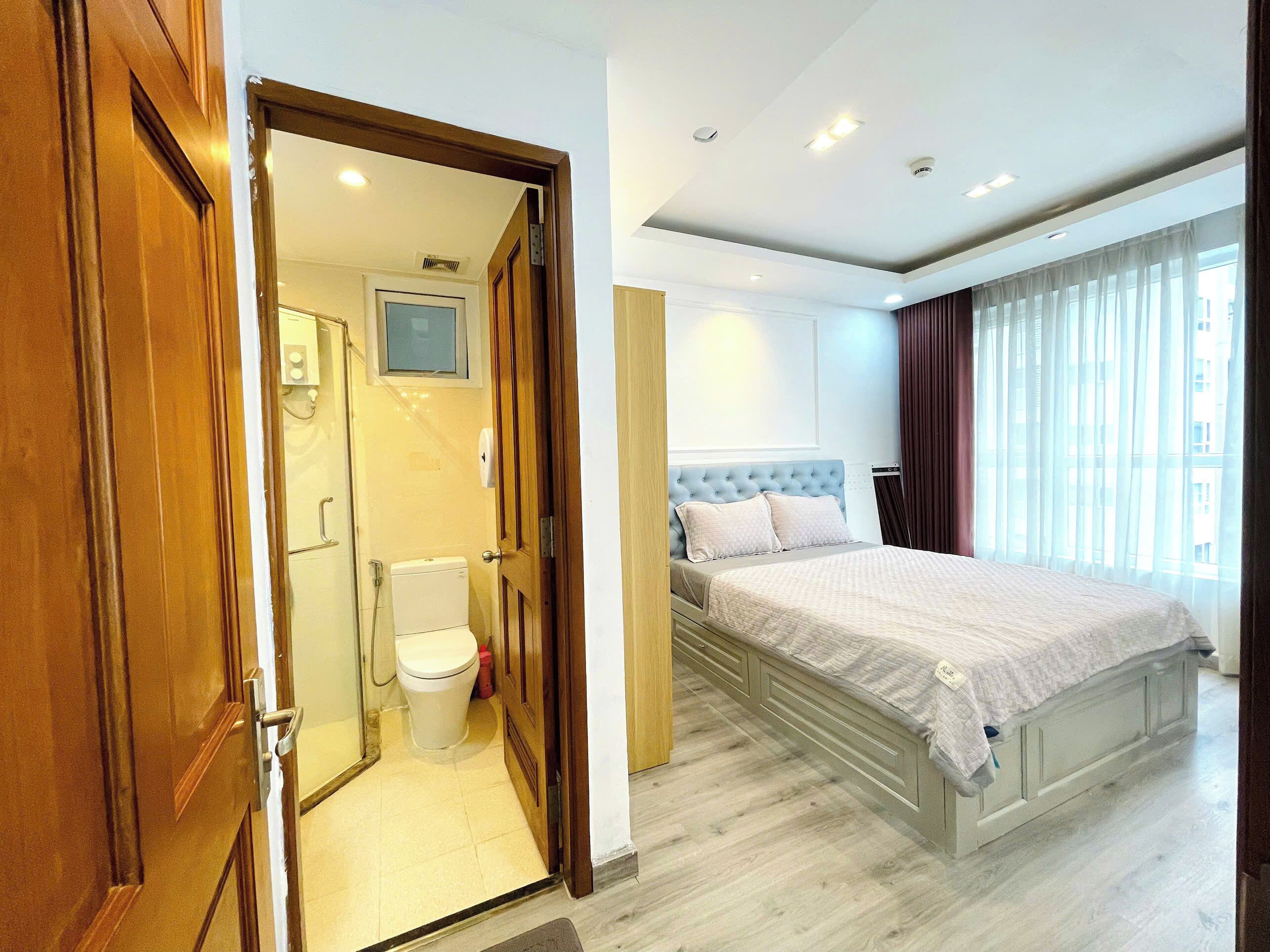 A hotel room with a large bed, a bathroom with a toilet and shower, and a view of the city through the window.
