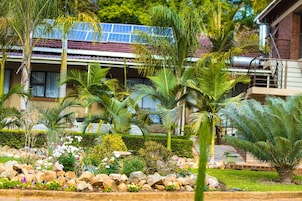Una casa con paneles solares, un jardín con diversas plantas y fachada de ladrillo.