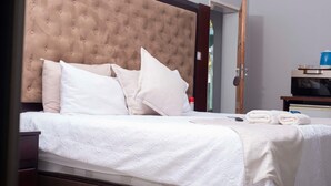 Una cama bien hecha con tablero de cabecera capitonado, ropa de cama blanca y un juego de toallas.