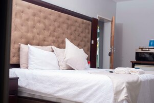 Una cama bien hecha con tablero de cabecera capitonado, ropa de cama blanca y un juego de toallas.