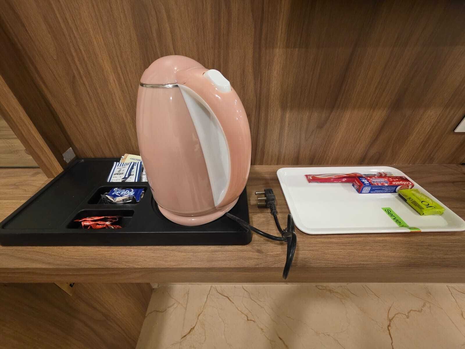 Una encimera de madera con una tetera rosa, una bandeja negra con aperitivos y una bandeja blanca con un paquete rojo y uno verde.