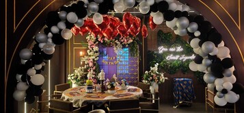 A decorated room with a round table, floral arrangements, and a neon sign.