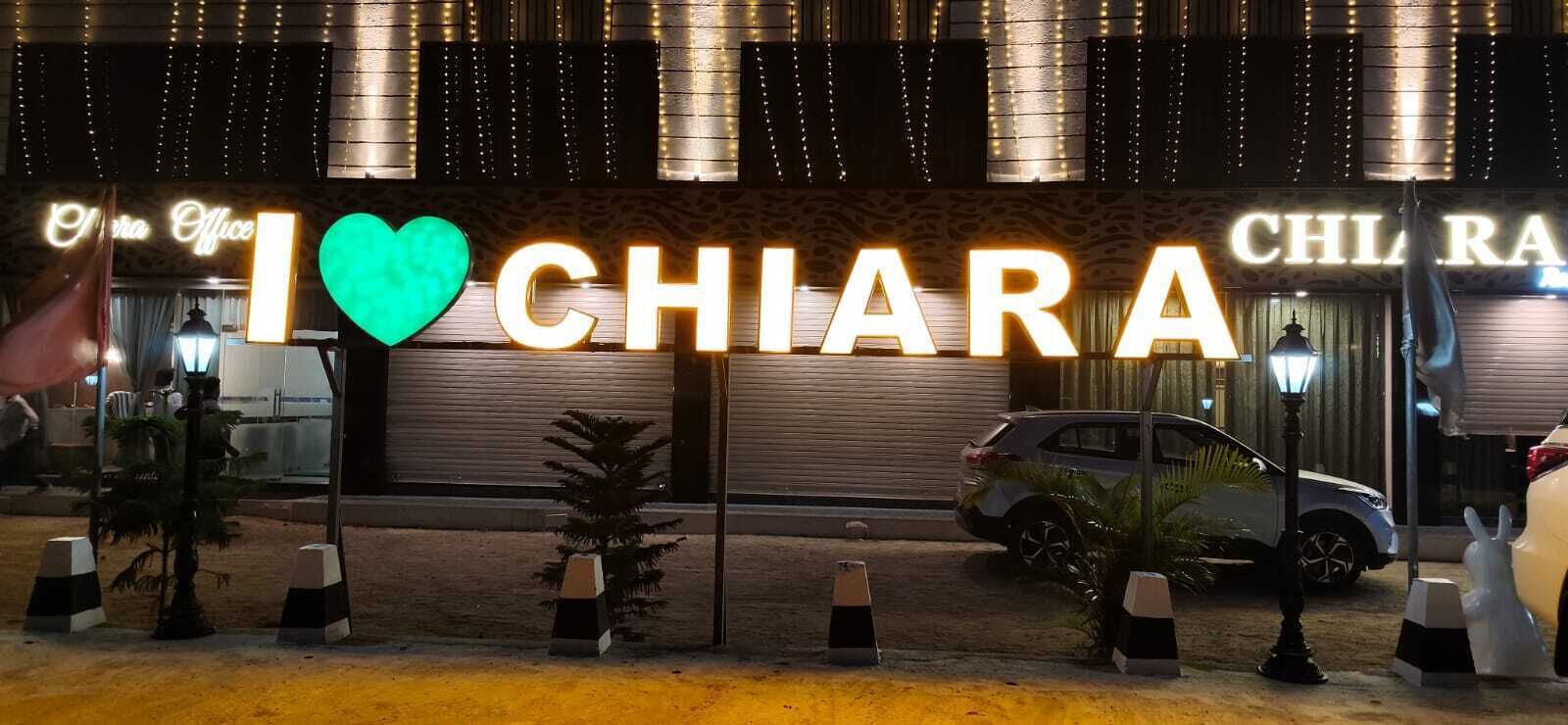 Entrada de hotel con señalización iluminada, zona de estacionamiento y pilares decorativos.
