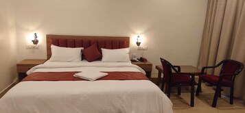 Une chambre d’hôtel comprenant un lit, deux tables de chevet, une chaise, une petite table et un rideau.