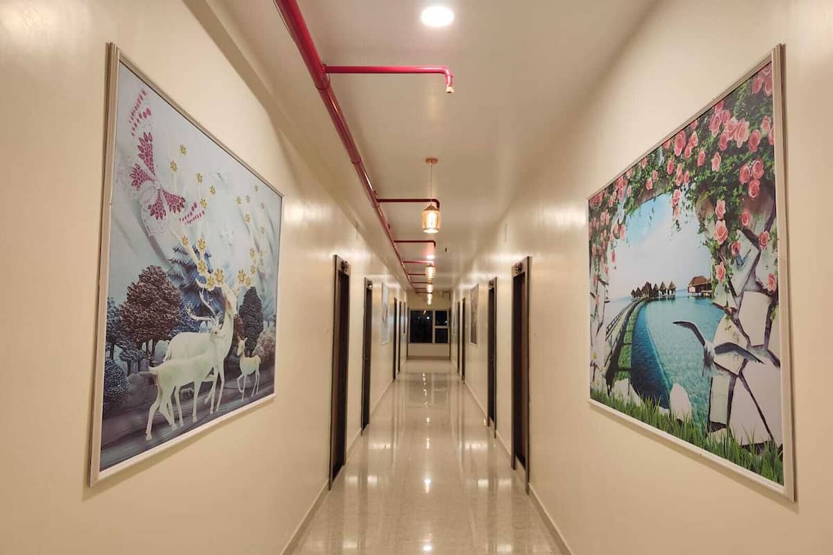 Corredor de hotel com um longo hall, obras de arte emolduradas nas paredes e um cano de teto vermelho.