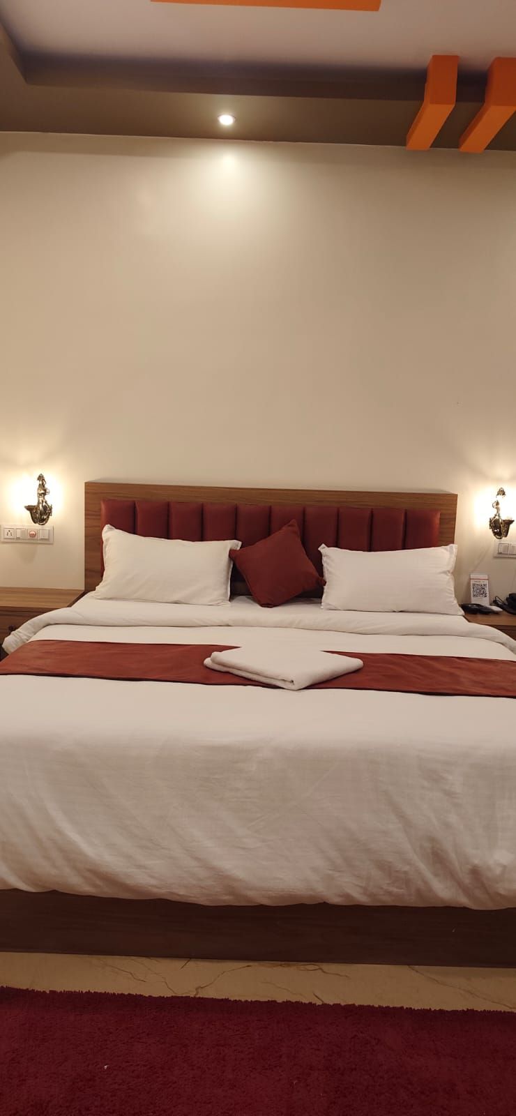 A neatly made bed with white and red bedding, a wooden headboard, and two bedside lamps.