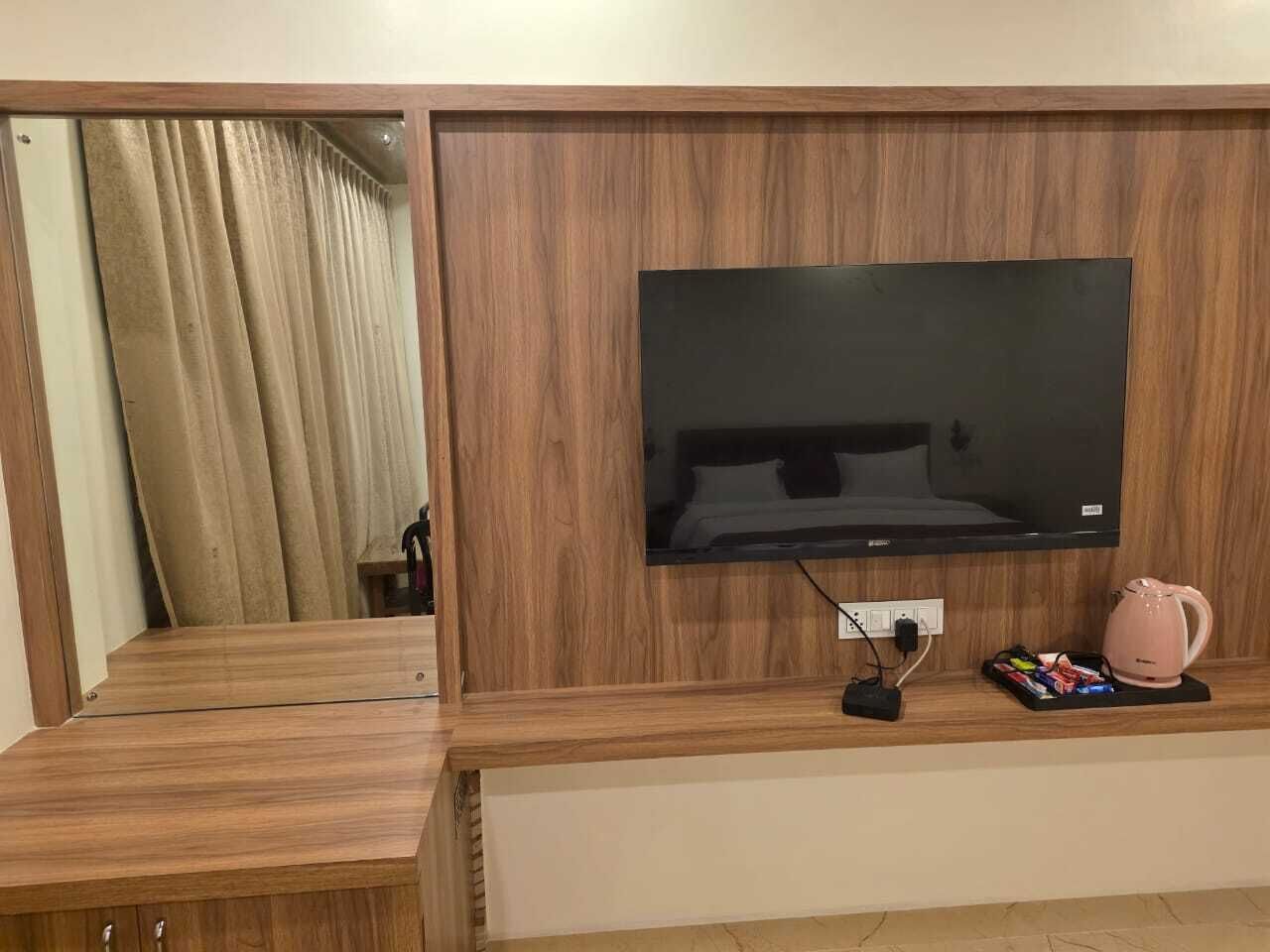 A wooden entertainment unit with a flat-screen TV, a power strip, and a pink kettle.