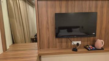 A wooden entertainment unit with a flat-screen TV, a power strip, and a pink kettle.