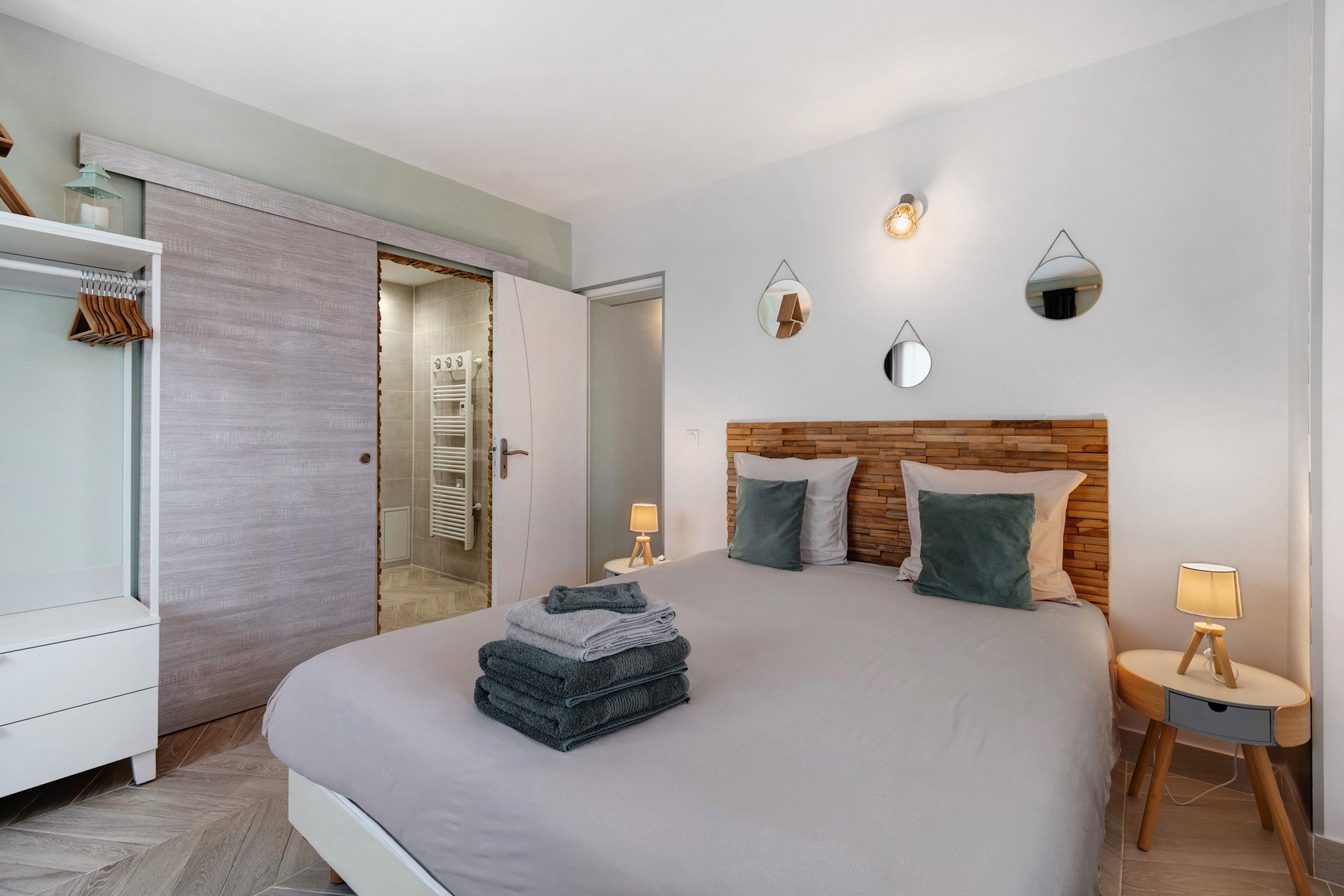 Une chambre moderne avec un grand lit, une armoire et une salle de bain visible à travers une porte ouverte.