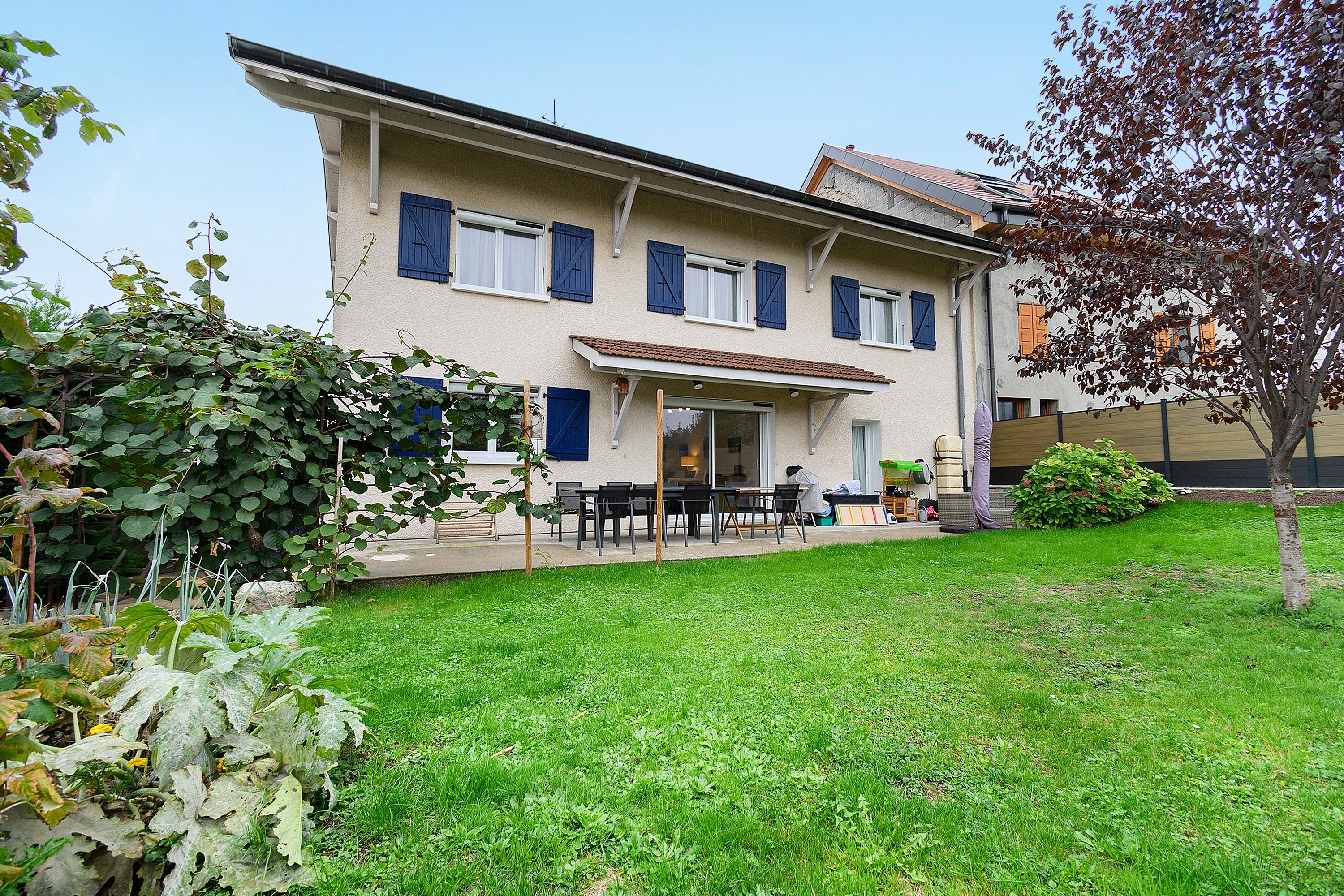Een tweelaags huis met een terras, een tuin en een boom.