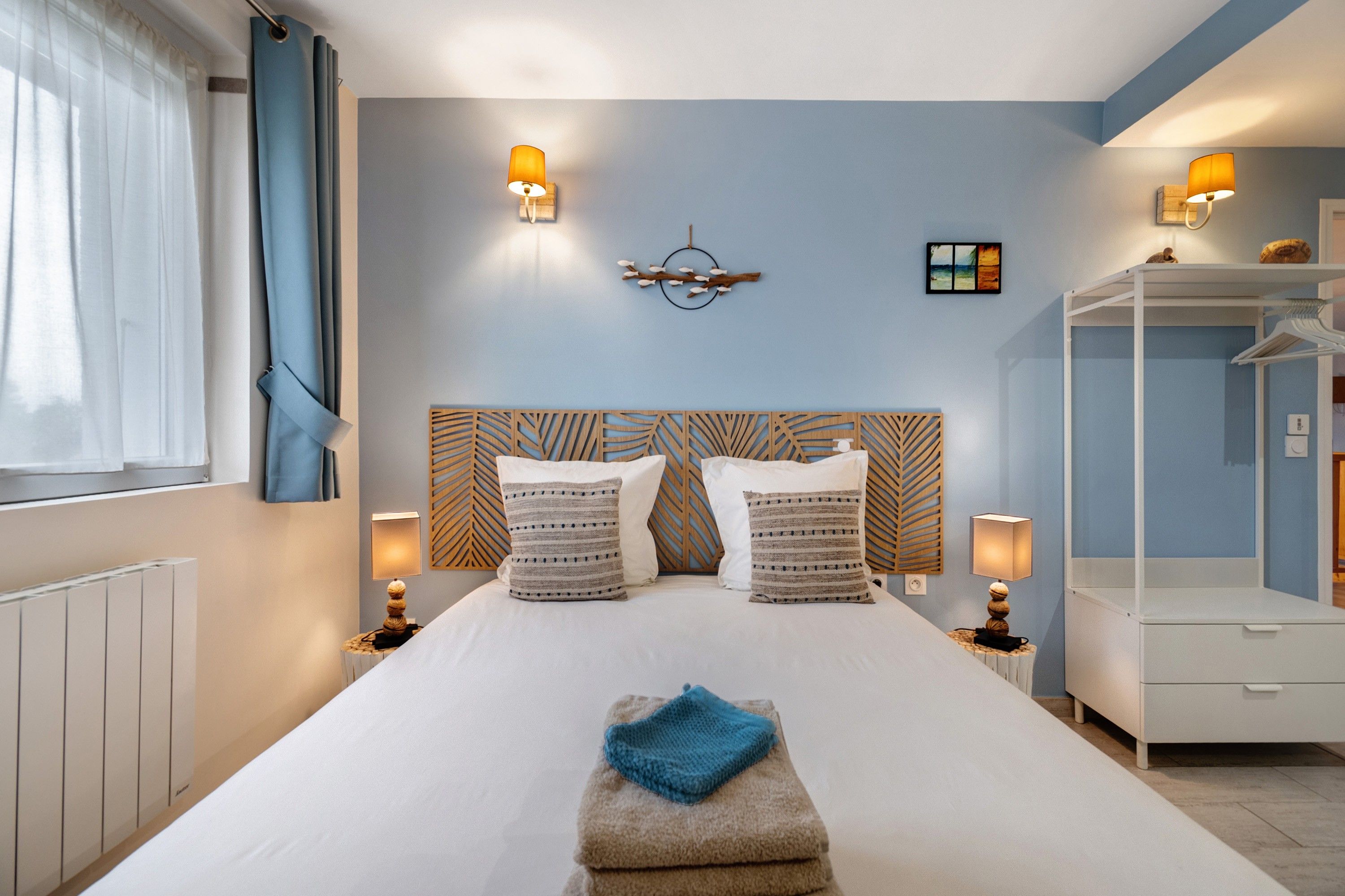Hotellihuone, jossa on sänky, yöpöytälamput, sängynpääty, seinätaideteos ja vaatekaappi.