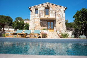Ein Gebäude aus Stein mit Pool, zwei Balkonen und Liegestühlen.