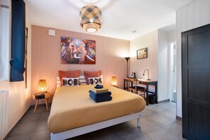 Een moderne slaapkamer met een bed, kunstwerken, bedlampjes, een bureau en een deur.