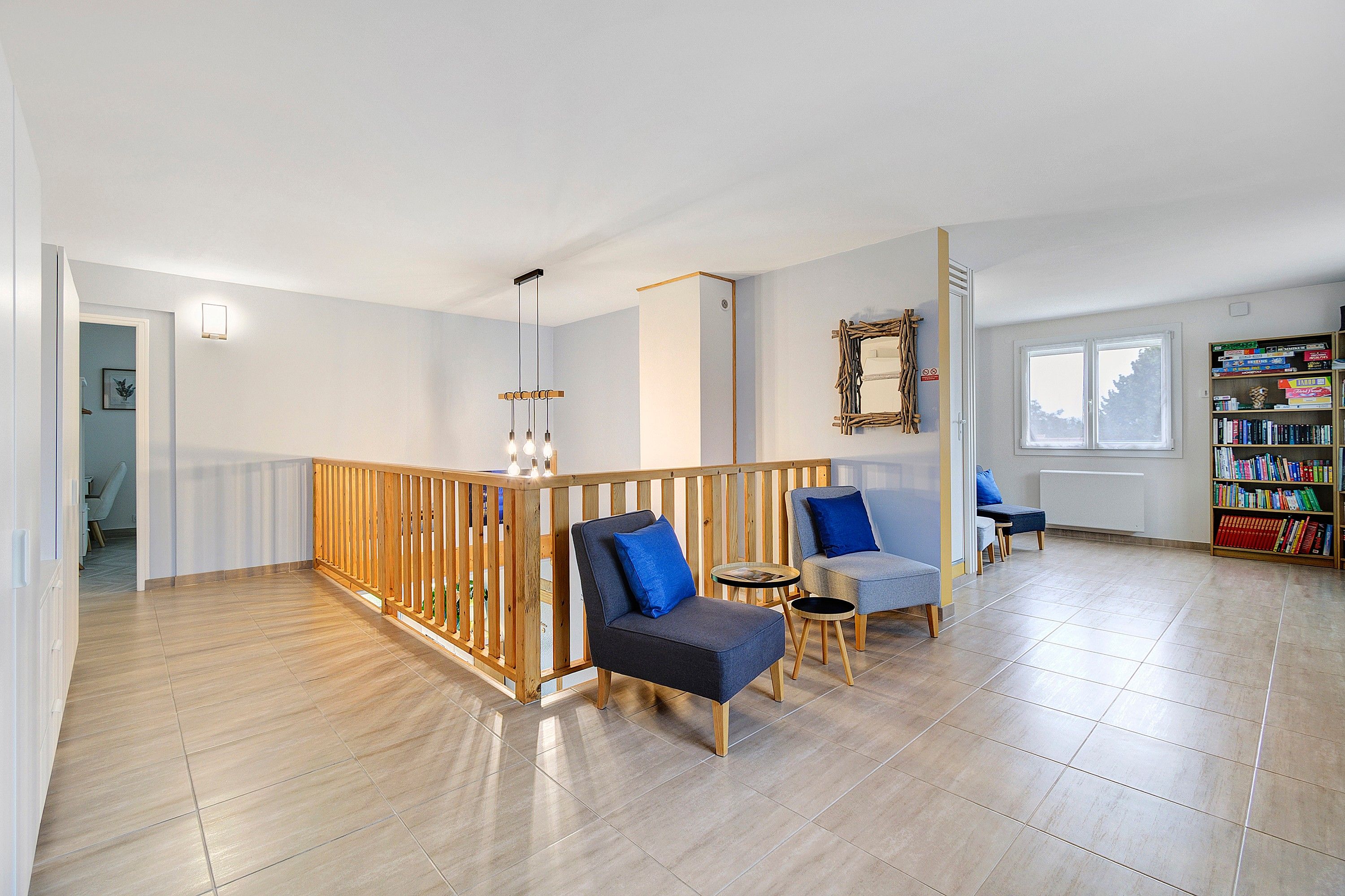 Een ruime woonkamer met houten balustrade, zitplaatsen, een boekenkast en een raam.