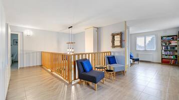 Een ruime woonkamer met houten balustrade, zitplaatsen, een boekenkast en een raam.