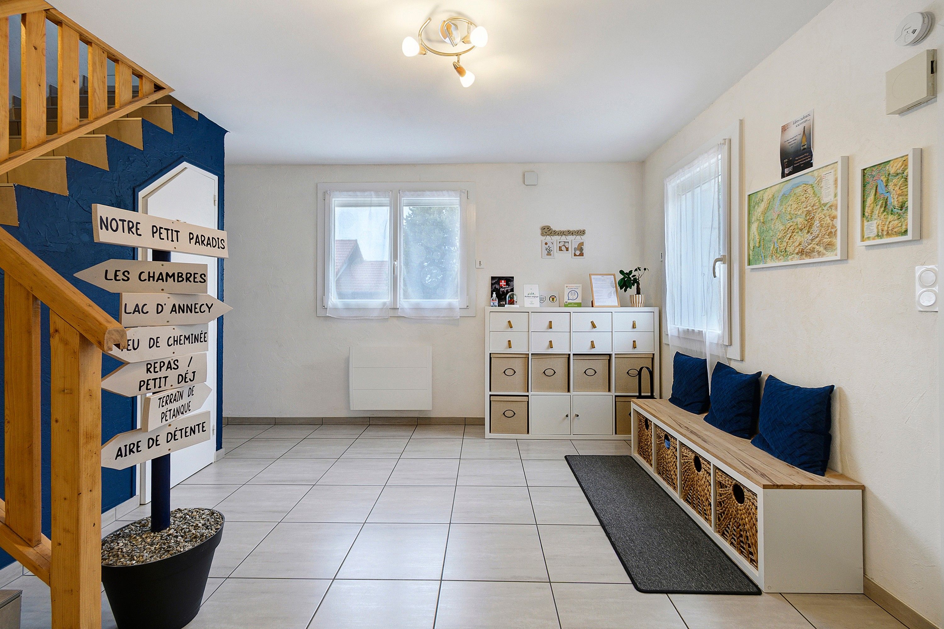 A spacious living room with a staircase, a white cabinet with drawers, a bench with cushions, and a wall with framed pictures.