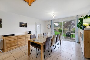 Un espace repas avec une table et des chaises en bois, un comptoir de cuisine, une grande fenêtre et une vue sur l’extérieur.