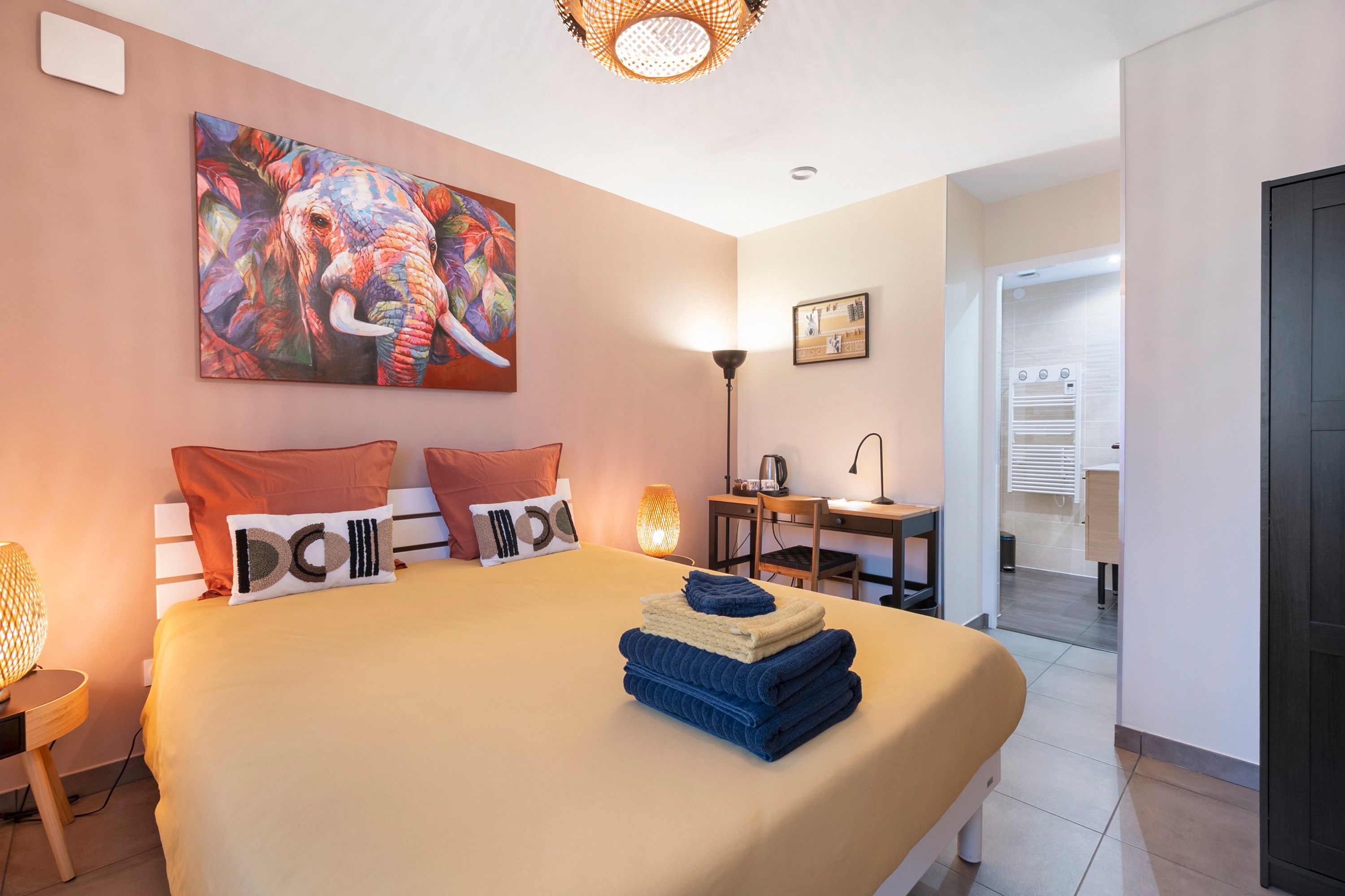 Una habitación de hotel con cama, escritorio, silla, lámpara y un cuadro en la pared.