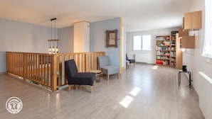 Un vaste espace de vie agrémenté d’une cloison en bois, de deux fauteuils, d’une petite table, d’une bibliothèque et d’une fenêtre laissant entrer la lumière naturelle.